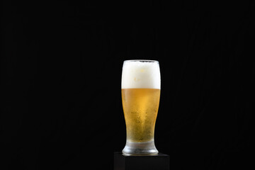 A glass of beer with a foamy head on a black background