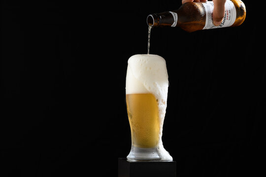 S&atilde;o Paulo, Brazil- May 08, 2023, hand holding non-alcoholic Budweiser beer bottle, full glass with foam on top, black background