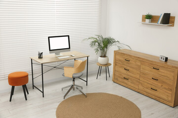 Stylish office interior with comfortable chair, desk, computer and houseplant