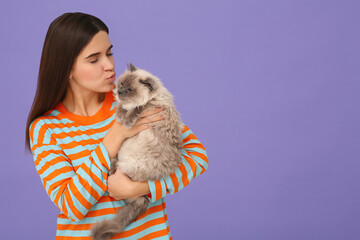 Woman kissing her cute cat on purple background, space for text
