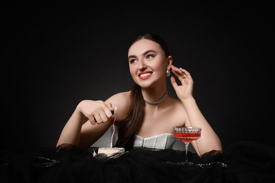 Fashionable photo of attractive young woman lighting candle on her Birthday cake against black background