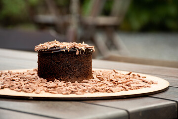 chocolate cake with chocolate shavings and chocolate cream on a rustic bistro table in a close-up garden at the blurred background outside