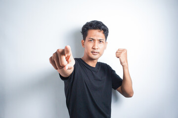 Fototapeta premium Asian young man in black t-shirt pointing forward, Looking at Camera, make choosing you gesture against white background