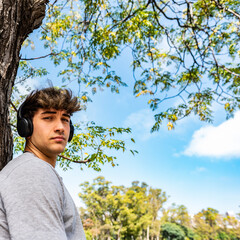 A young man listening to music while leaning on a tree