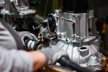 Worker connects car engine gearbox details on shop conveyor