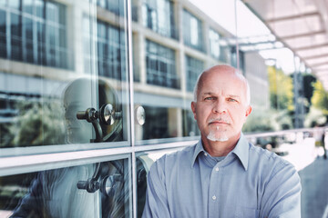 Proud senior leaning against the glass wall of his company.