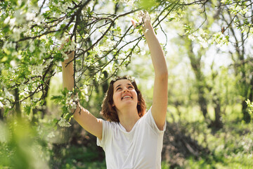 Beautiful teenage girl with spring flowers enjoying nature and laughing on spring garden. Girl holding branch of an cherry tree. Freedom and happiness concept. Springtime.