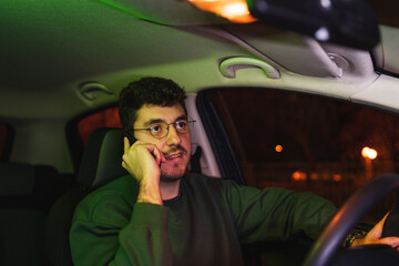 One young man is working from car in backseat while using laptop and mobile phone to work during the night