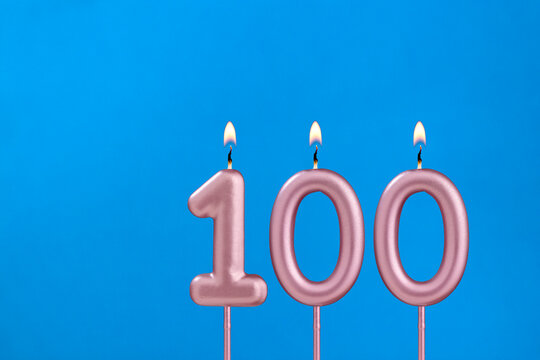 Number 100 - Burning anniversary candle on blue foamy background
