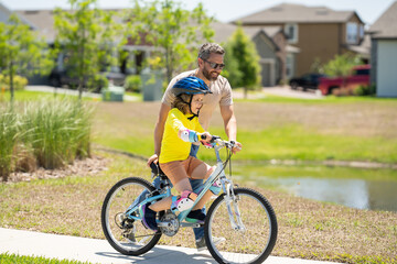 Fototapeta na wymiar Happy Fathers day. Father and son in a helmet riding bike. Little cute adorable caucasian boy in safety helmet riding bike with father. Family outdoors summer activities. Childhood and fatherhood.