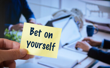 Male hand holding sticky note written Bet on yourself.
