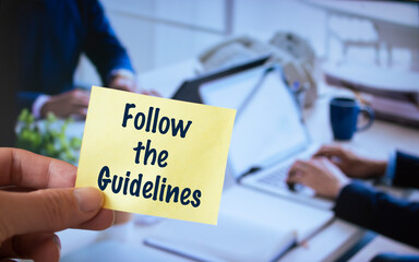 Male hand holding sticky note written Follow The Guidelines.