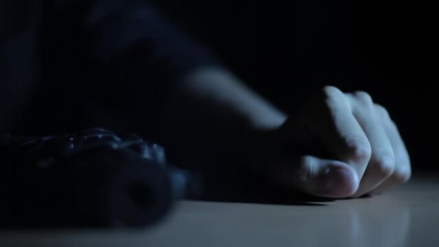 Close-up shot of a man picking up a gun from a table, creative light cinematic shot HD footage.
