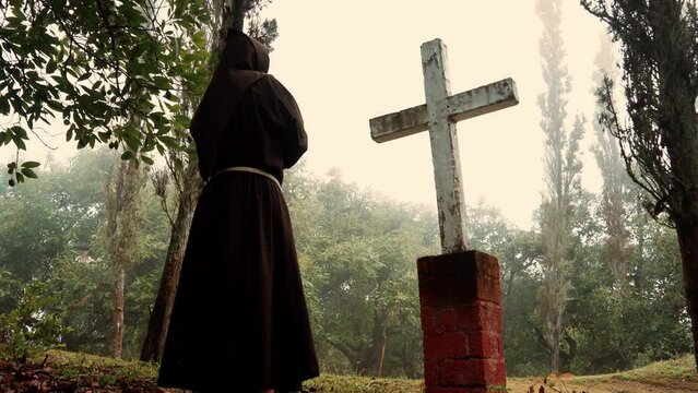 Fraile Franciscano monje meditando y contemplando la cruz sobre terreno campo en montaña en un día nublado al amanecer al aire libre en el bosque