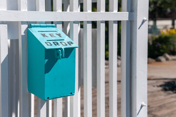 Blue key drop box on an outdoor area hung on a white wood fence