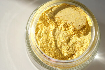 An open jar of a yellow turmeric facial scrub showing off its texture.