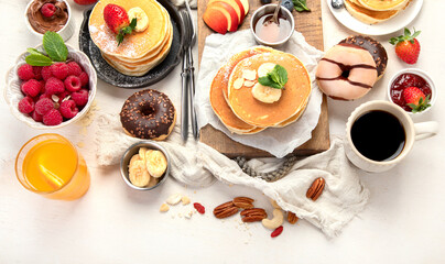 Pancakes with fresh fruits, donuts and coffee on a white background.