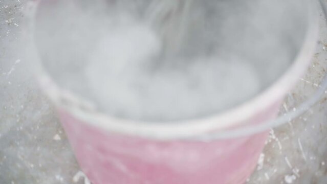 Dry powdered cement is poured into a plastic bucket, close-up