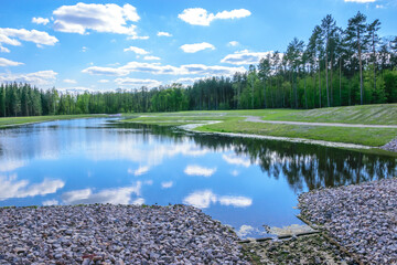 Fototapeta Piękny widok, błękitne niebo z gęstymi chmurami odbijającymi się w tafli wody w otoczeniu zieleni obraz