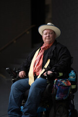 A middle-aged man sits in his wheelchair, and turns to look at the camera with a confident smile. He is outside a stairwell at an office building, highlighting a theme of accessibility.