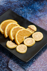 Plate of orange cut into segments, with guavas around it black Plate,