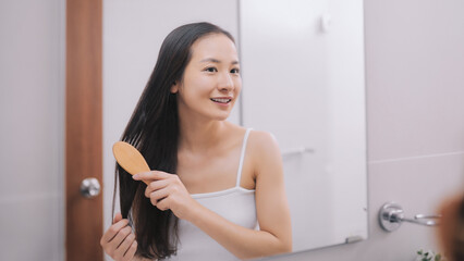 Happy attractive young woman combing wet hair with comb in bathroom after shower at home. Hair care and healthy hair