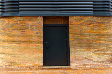 Black metal door in the red brick wall with a smooth transition to the sidewalk