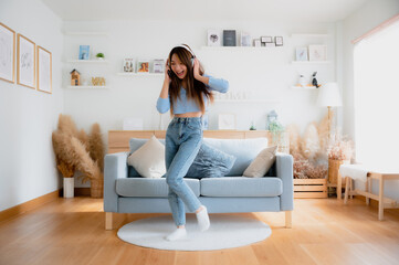 Young asian woman dancing in living room. Asian woman with a smile relaxing at home, happy and in good mental and physical health, wearing headset and listening to music