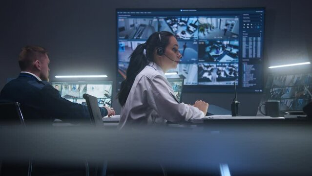 Female operator types keyboard and monitors security cameras with AI facial recognition in police surveillance room. PC monitors and big digital screens on the wall with displayed CCTV cameras view.