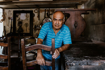 latin senior man carpenter working on wood chair at the furniture workshop in Mexico Latin America, hispanic worker in carpentry