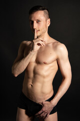 Naklejka premium Young attractive man with an athletic body on a black background.
