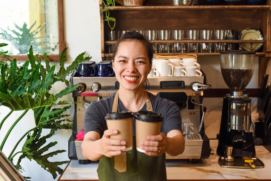 Vietnamese smiling waitress holding paper cups with coffee in a cafe