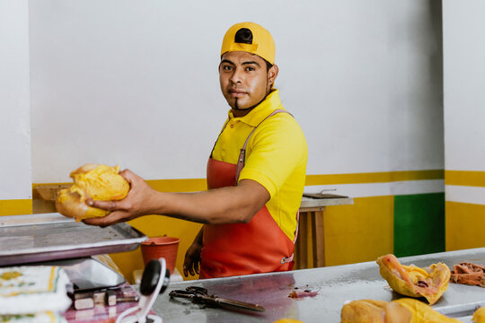 Latin man working as Poultry vendor of raw chickens being sliced by the Pollero at Chicken shop or Polleria in Mexican market in Mexico, Hispanic people working