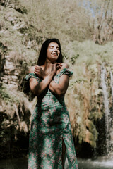 Beautiful model in a turquoise dress posing near a mountain waterfall.Wildlife concept