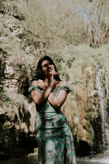 Beautiful model in a turquoise dress posing near a mountain waterfall.Wildlife concept