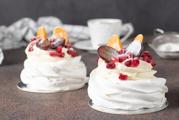 Mini Pavlova cake with pomegranate, tangerines and grapes on brown background