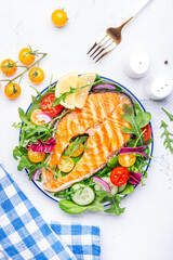 Grilled salmon steak with vegetable salad with tomatoes, arugula, onion  and lettuce on plate, gray table background, top view