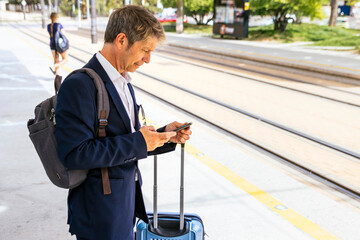 Businessman waiting for the train checks the timetable on the phone