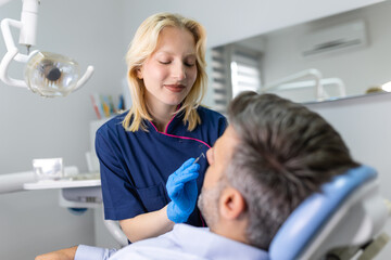 Obraz premium Dentist in blue uniform doing teeth procedure to patient, male patient during treatment procedure in contemporary dental clinic