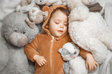 Little baby with outstretched hands lying in bed with fluffy stuffed toys of animals. Toddler sleeping with teddy bear in cozy room and enjoy healthy night sleep. Selective focus. 