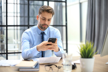 Handsome businessman in office using smartphone.