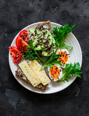 Sandwiches with avocado, cheese, seeds,  boiled egg, tomato and green salad - delicious breakfast, snack on a dark background, top view