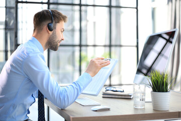 Young man is working with papers while sitting in the office. Successful entrepreneur is studying documents with attentive and concentrated look