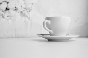 Black and white photo of white cup in front of brick wall. Cup with copy space