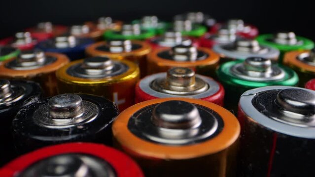 Camera focuses on discarded alkaline batteries, often used in portable electronics. Filmed in macro on a dark surface.
