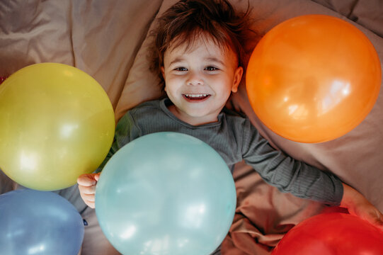 Happy boy lying on bed amidst balloons