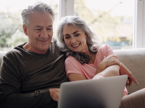 Happy senior couple with laptop relaxing on couch at home