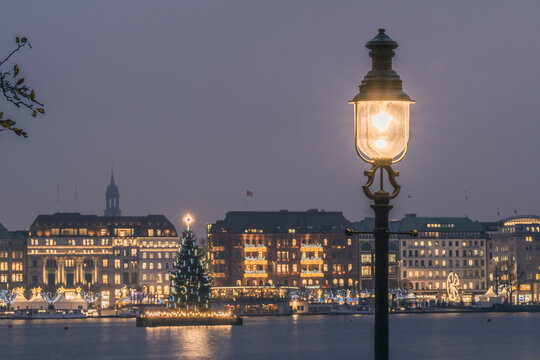 Germany, Hamburg, Street light glowing in front of Alster Lake at dusk with Christmas tree in background
