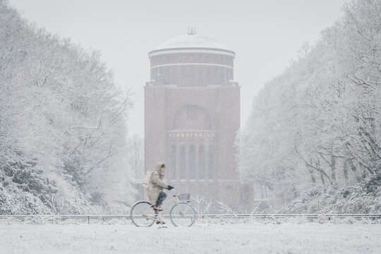 Germany, Hamburg, Person riding bicycle past Stadpark planetarium during heavy snowfall