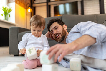 Bearded father playing with toddler child on floor with cubes.